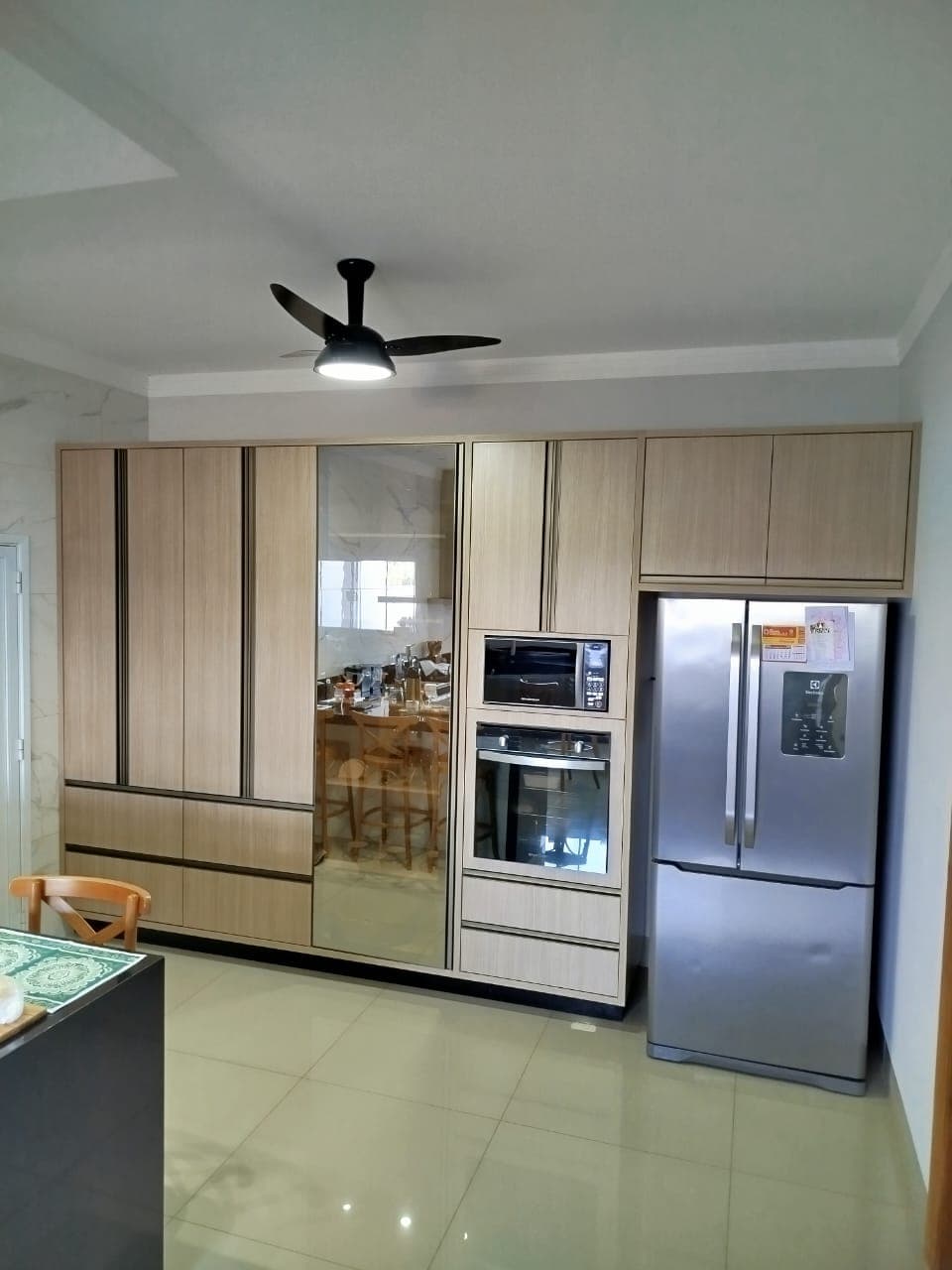 Cozinha em tom amadeirado claro com porta espelhada e geladeira inox